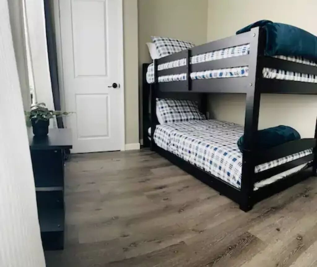 Una cama litera con ropa de cama a cuadros, una manta oscura y una planta en maceta sobre un suelo de madera.
