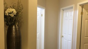 A hallway with dark wooden flooring, white doors, and a vase with flowers on a shelf.