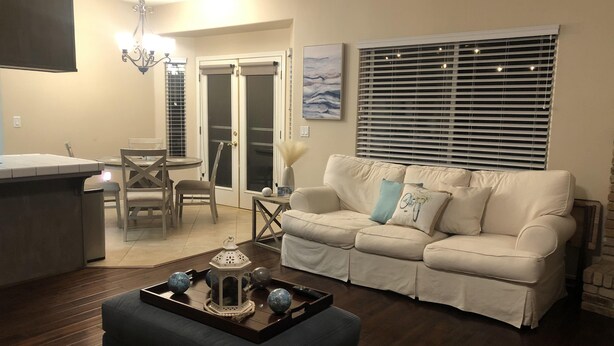 A living room with a sofa, a coffee table with decorative items, a dining area with a table and chairs, and a kitchen area with a counter.