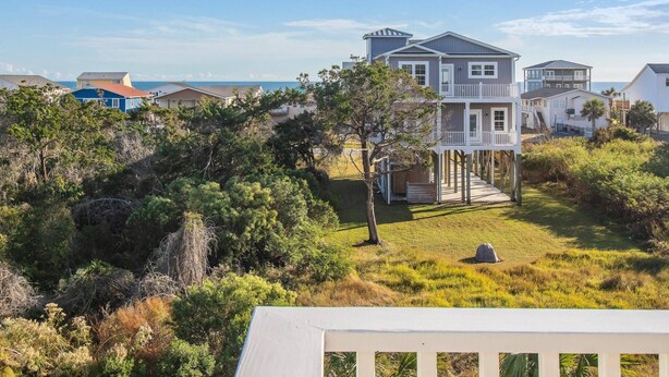 A coastal house with a balcony, surrounded by lush greenery and a view of the sea. - Wonderful Ocean Views - Sleeps 12 -3 Mins to Beach (Oak Island)