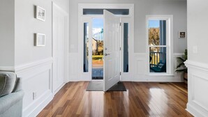 A hallway with wooden flooring, white walls, and a door leading to an outdoor area with a view of a house and trees. - Wonderful Ocean Views - Sleeps 12 -3 Mins to Beach (Oak Island)
