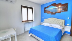 Une chambre à coucher avec un lit, une fenêtre, un radiateur, un bureau et un mur orné d’un tableau.