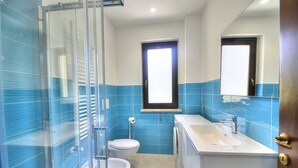 Une salle de bain avec une douche à parois de verre, des toilettes, un lavabo et une fenêtre.