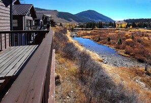 A wooden deck overlooking a river with autumn foliage and mountains in the background.