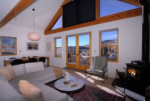 Un salón amplio con chimenea, sofá, mesa de comedor y ventanas grandes con vistas al exterior.