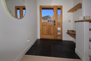 A hallway with a wooden door, a mirror, a shelf with baskets, and a view of a house and mountains.