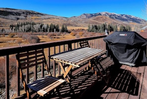 Une terrasse en bois avec un barbecue et des bancs, offrant une vue sur un paysage montagneux.