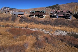 Un quartier résidentiel composé de plusieurs maisons, traversé par un ruisseau, avec une chaîne de montagnes en arrière-plan.