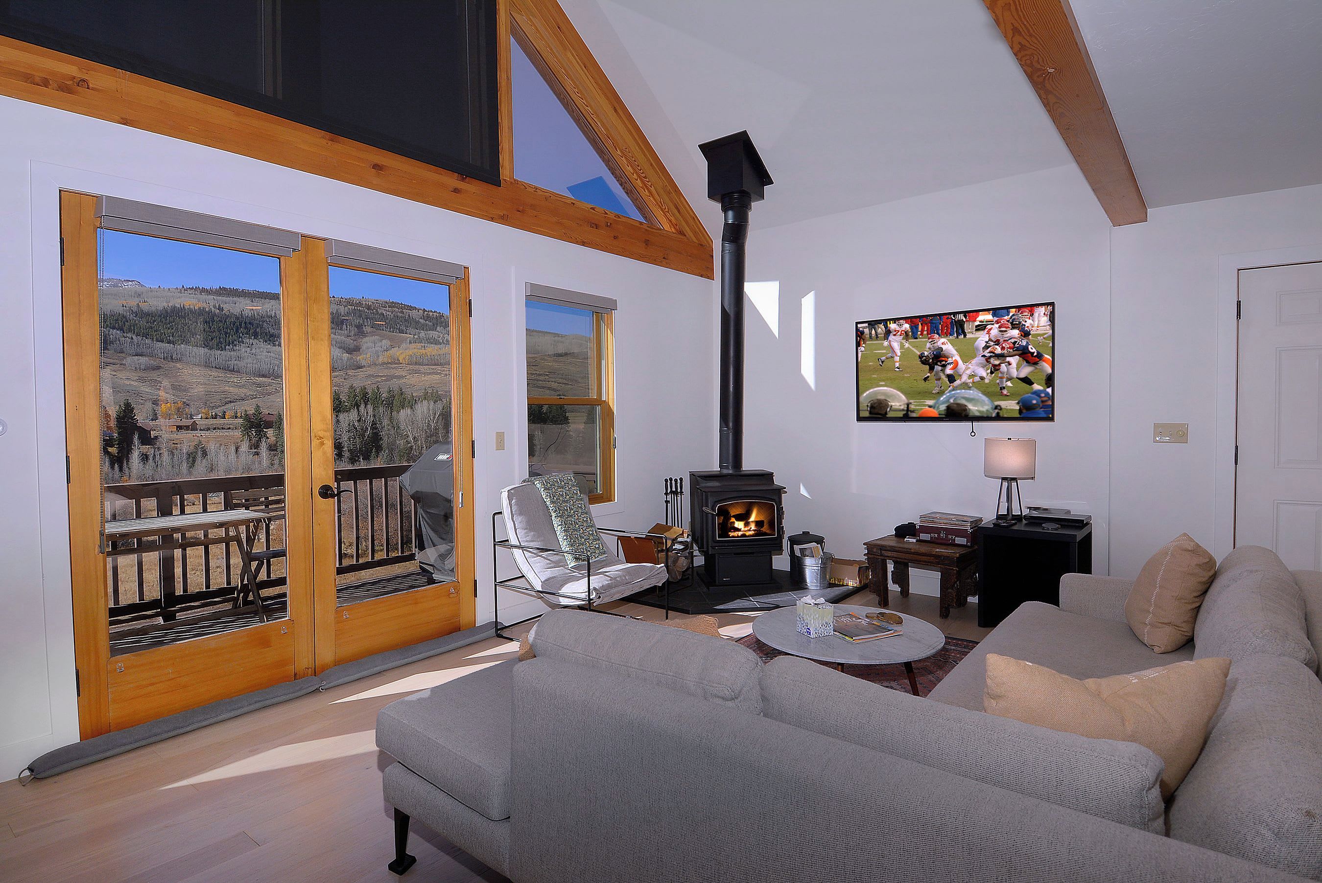 A living room with a fireplace, a sofa, a television, and a view of a mountainous landscape through large windows.