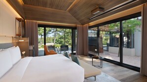 Habitación de hotel moderna con una cama grande, zona de estar y vistas al exterior, además de un ventanal amplio.