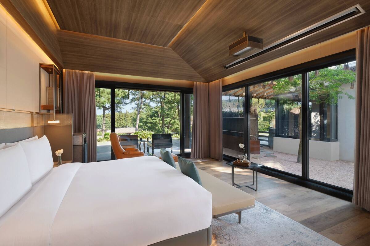 A modern hotel room with a large bed, a seating area with a view of the outdoors, and a large window.