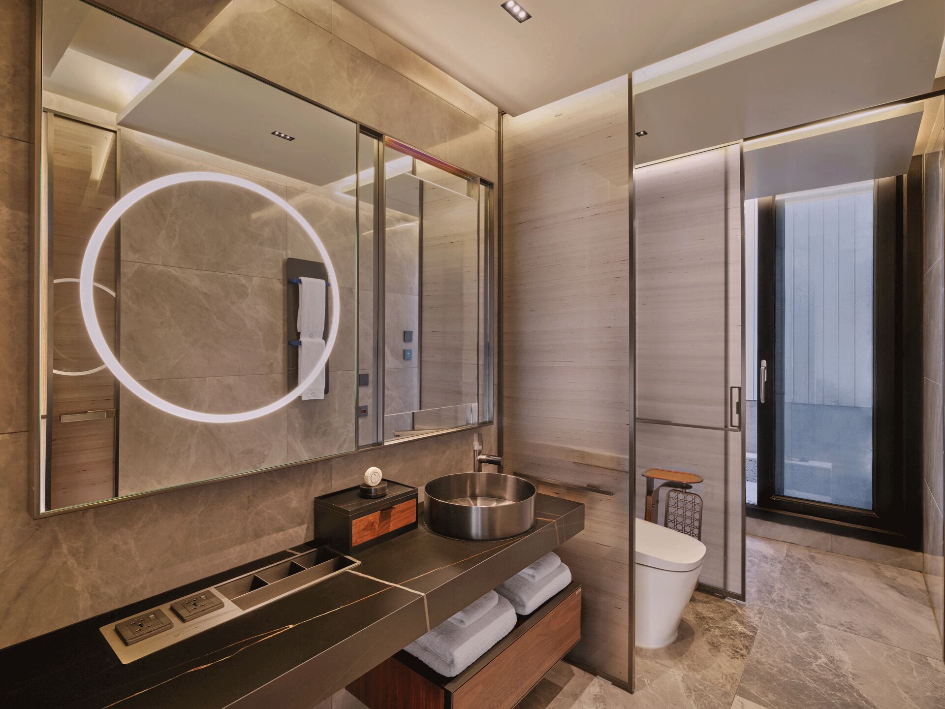 Une salle de bain moderne avec un grand miroir, un luminaire rond, un lavabo et des toilettes.