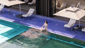 Zona de piscina con sillones de descanso y sombrillas.