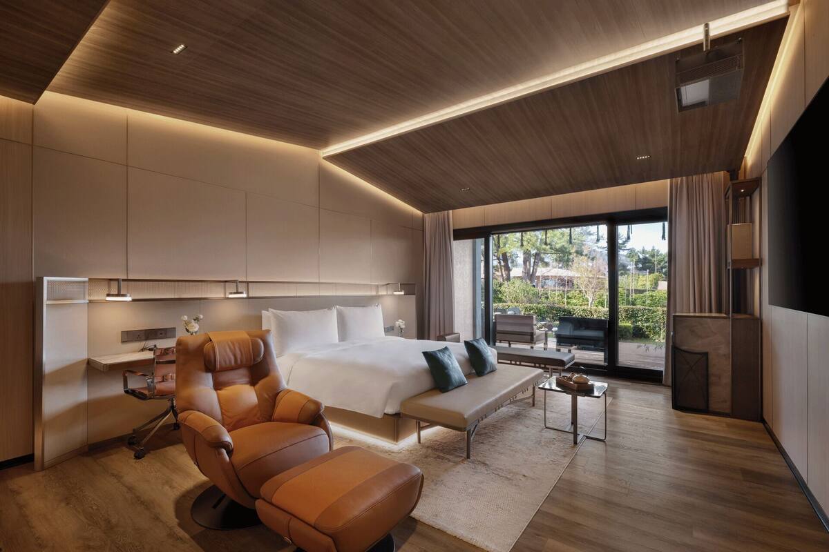 A modern hotel room with a large bed, a leather armchair, a sofa, and a dining area.