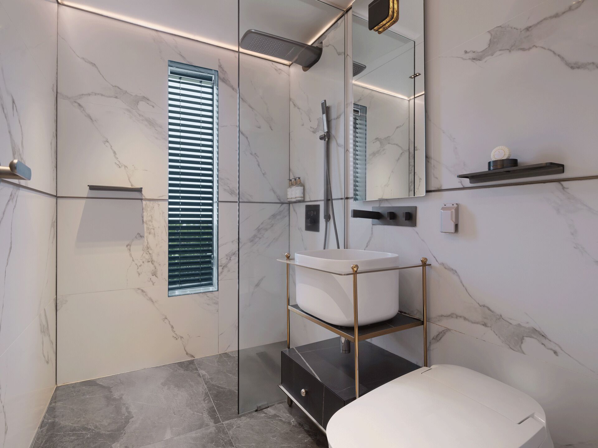 Un baño moderno con lavamanos blanco, cabina de ducha con vidrio y pared revestida de mármol.