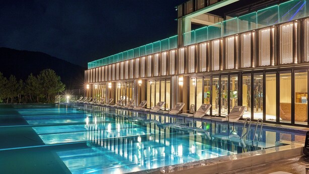 Un hotel moderno con una amplia piscina al aire libre, sillas de descanso y fachada de vidrio.