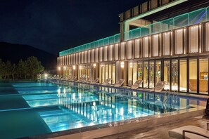 A modern hotel with a large outdoor swimming pool, lounge chairs, and a glass facade. - Amber Pure Hill Hotels & Resorts Jeju (Jeju City)