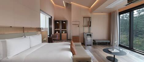 A modern hotel room with a large bed, a seating area, a small table, and a view of the outdoors.