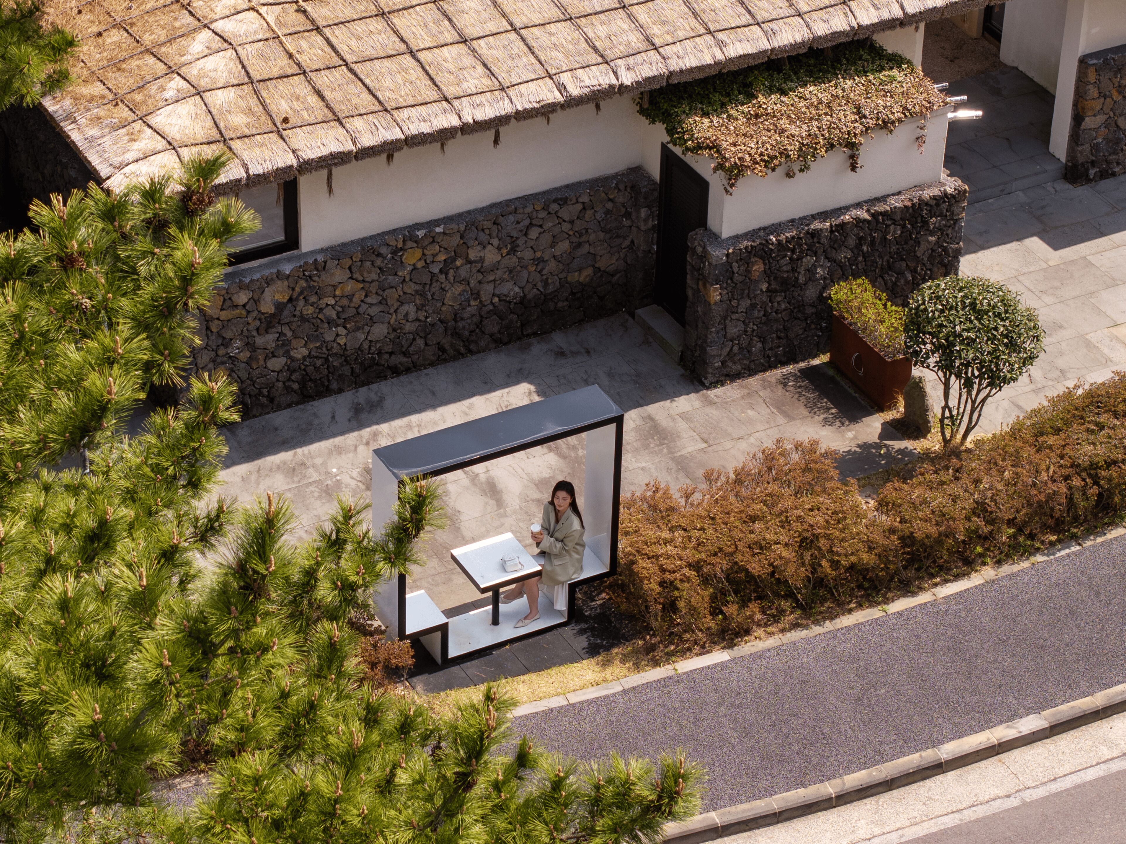 Un bâtiment moderne avec une façade en pierre, un toit de chaume et un banc avec une table.