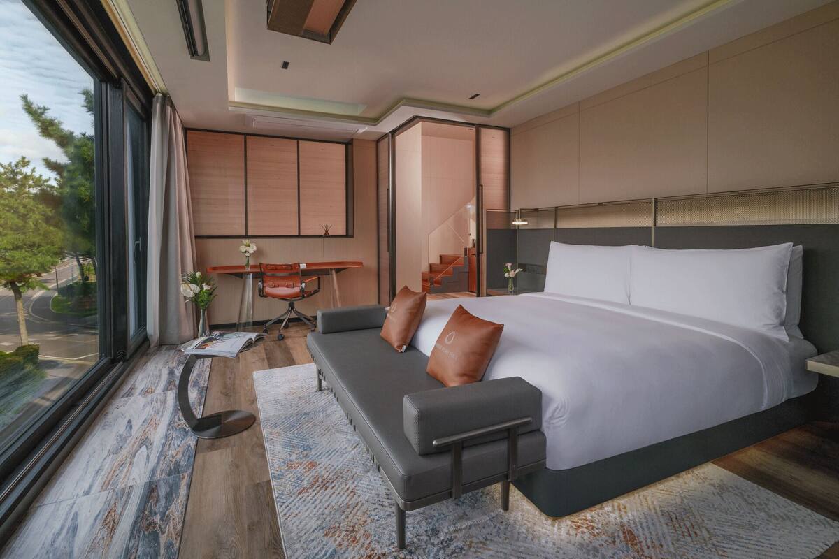 A modern bedroom with a large bed, a sofa, a desk, and a view of the outdoors.