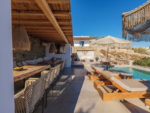 A poolside area with wooden lounge chairs, a dining table, and a stone wall.