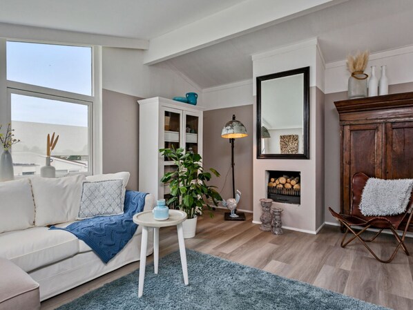 A modern living room with a sofa, a small table, a potted plant, a floor lamp, a fireplace, and a large mirror.
