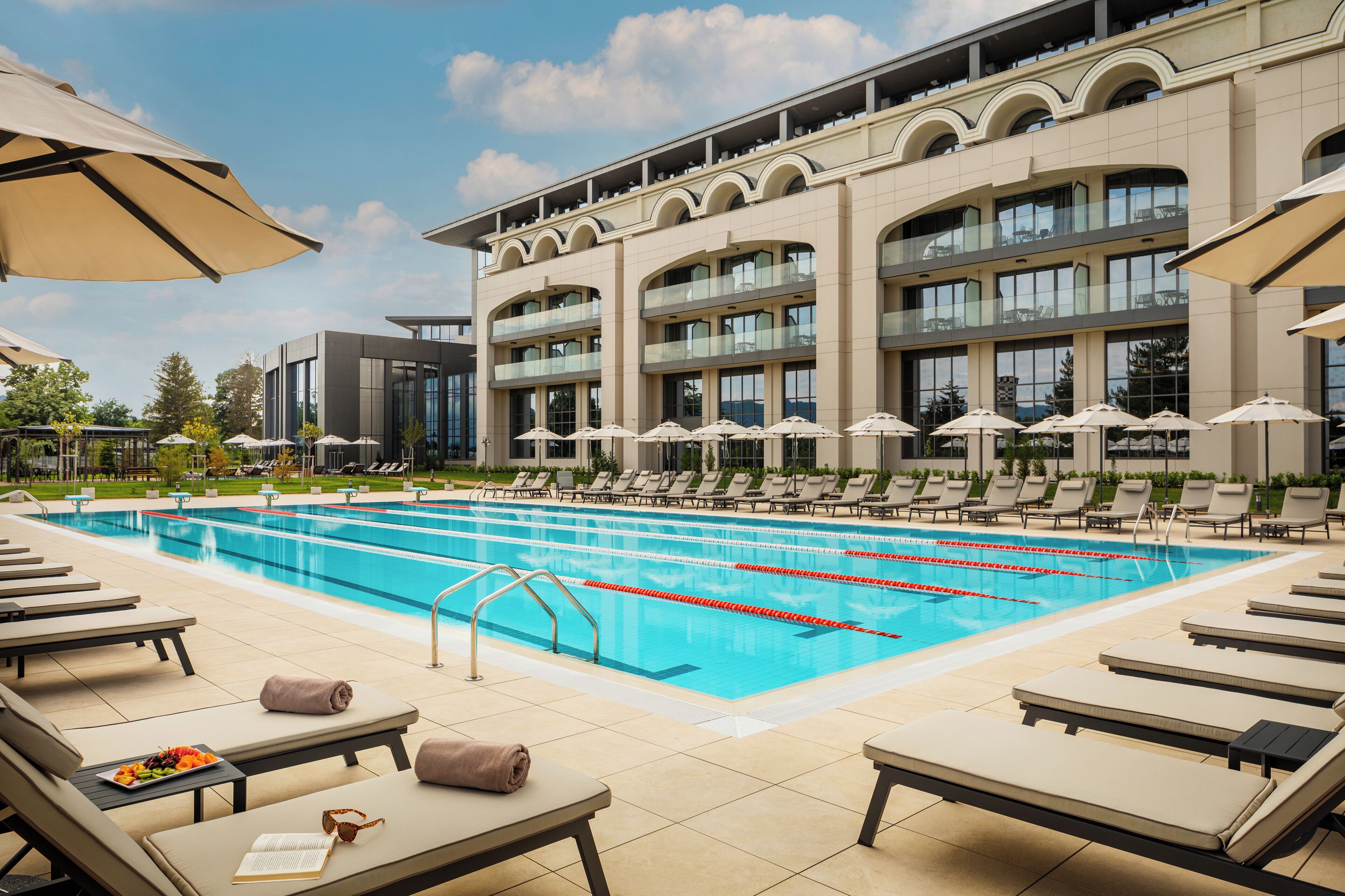 A swimming pool with lounge chairs and umbrellas, surrounded by a building with multiple balconies.