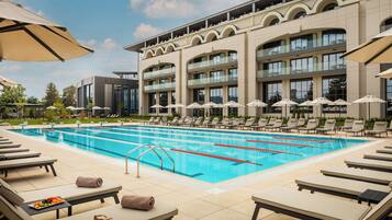 A swimming pool with lounge chairs and umbrellas, surrounded by a building with multiple balconies.