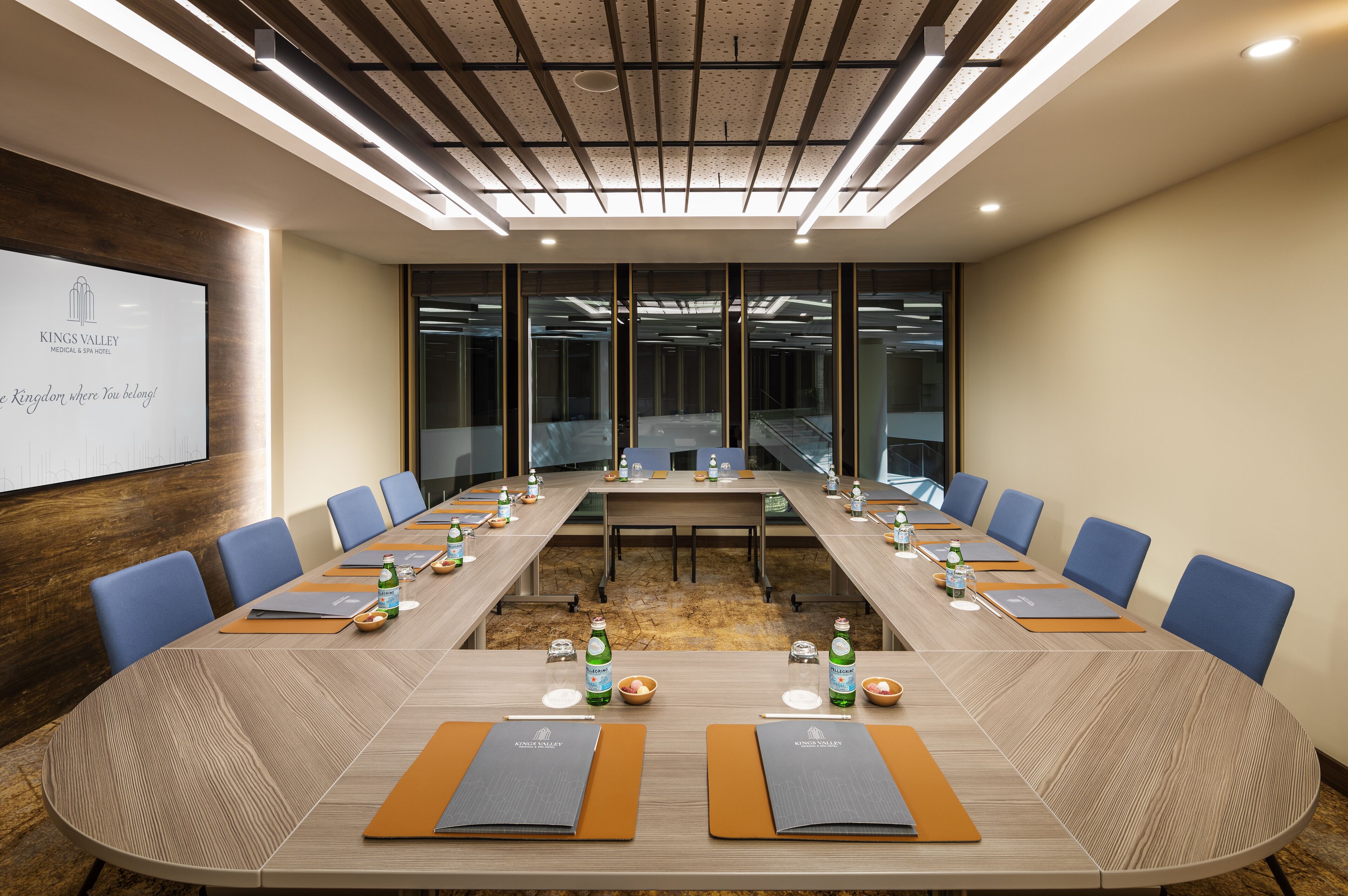 Une salle de conférence avec une longue table, des chaises bleues et un écran de projection affichant le nom « Kings Valley Hotel & Spa ».