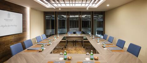 A conference room with a long table, blue chairs, and a projector screen displaying "Kings Valley Hotel & Spa".