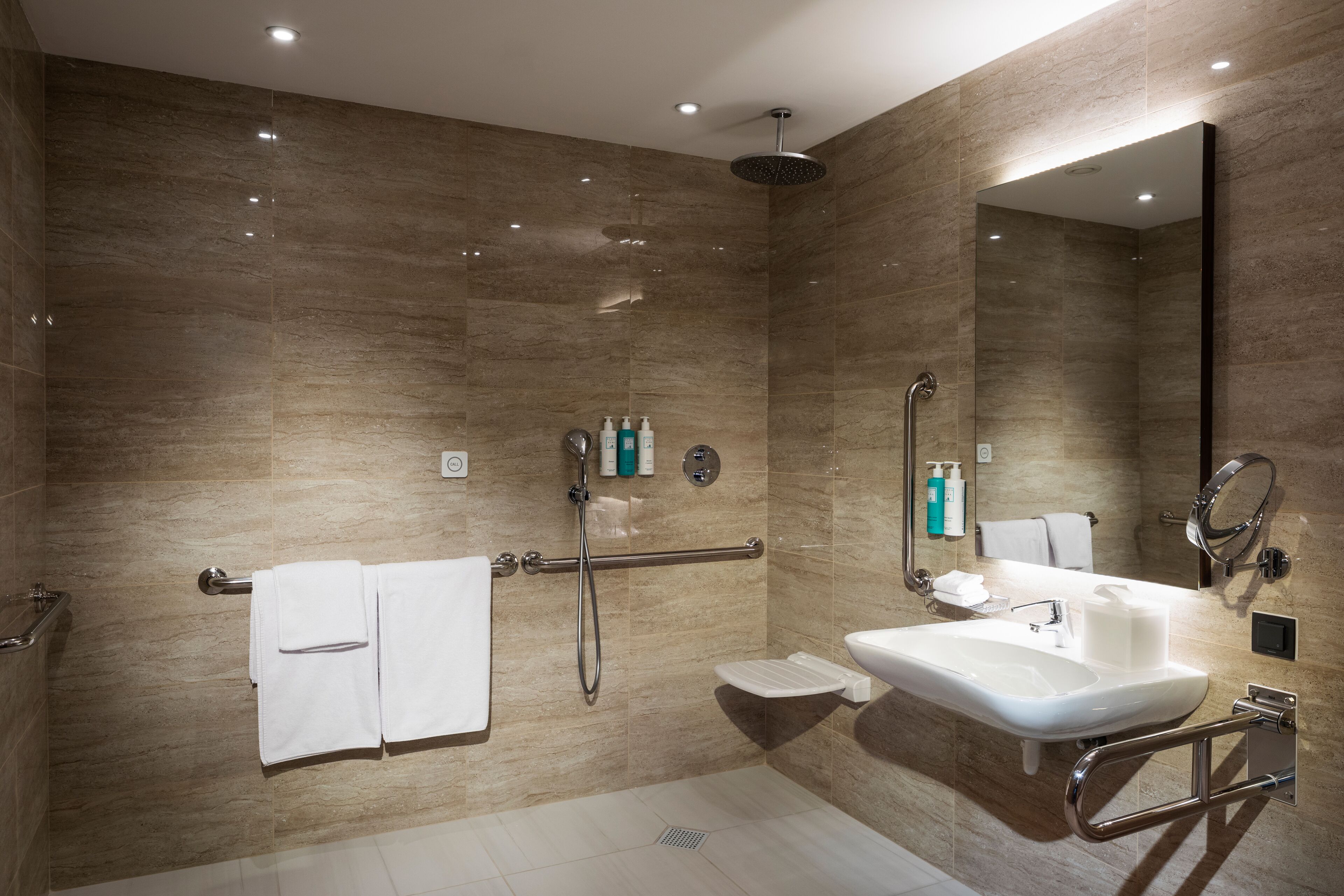 A modern bathroom with a shower, sink, and handrails.