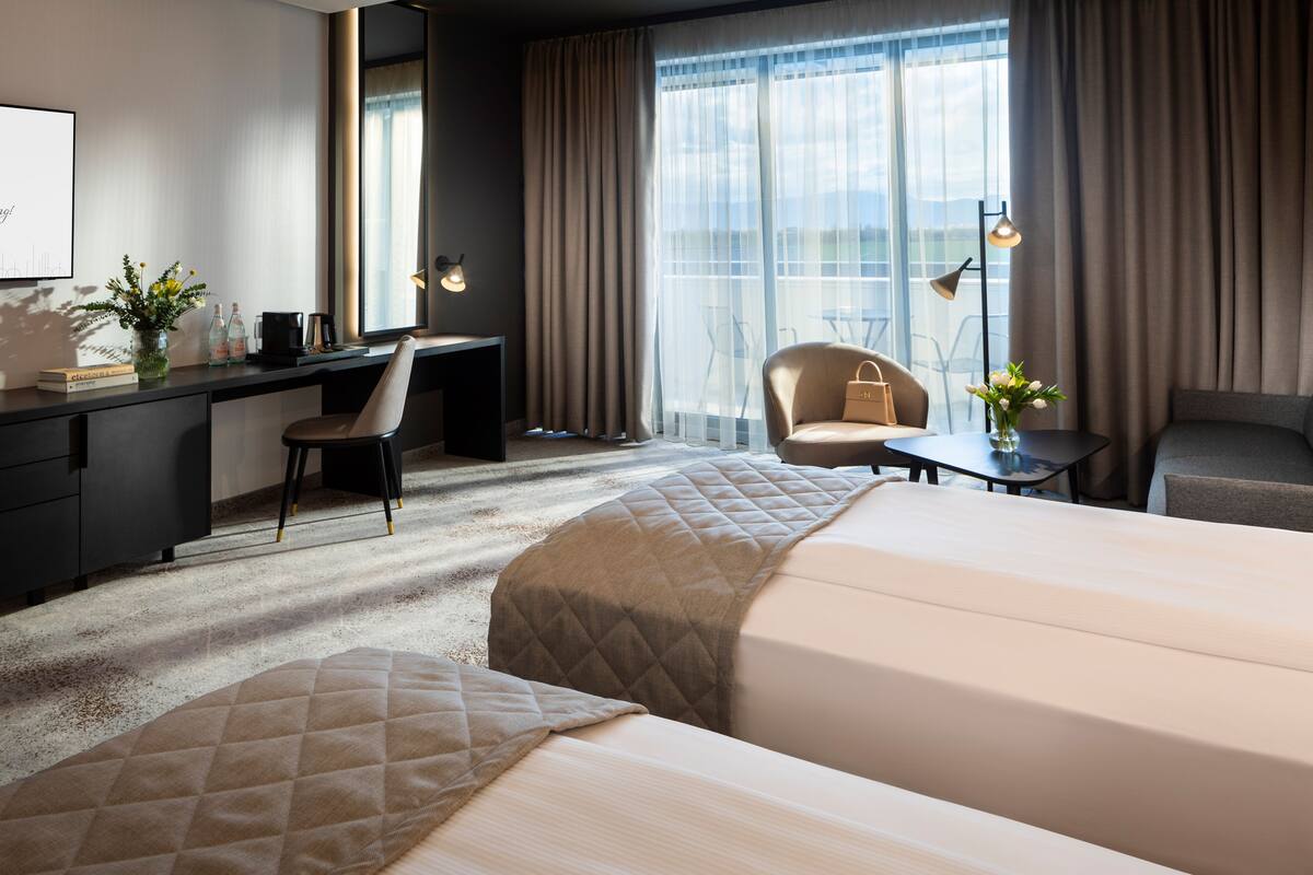 A hotel room with a bed, a desk, a chair, a small table, and a view of the outdoors.