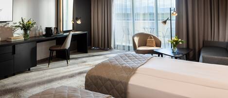 A hotel room with a bed, a desk, a chair, a small table, and a view of the outdoors.