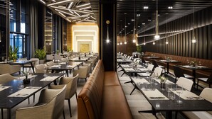 A modern restaurant interior with long tables, booths, and a central seating area. - Kings Valley Medical & Spa Hotel (Kazanlak)