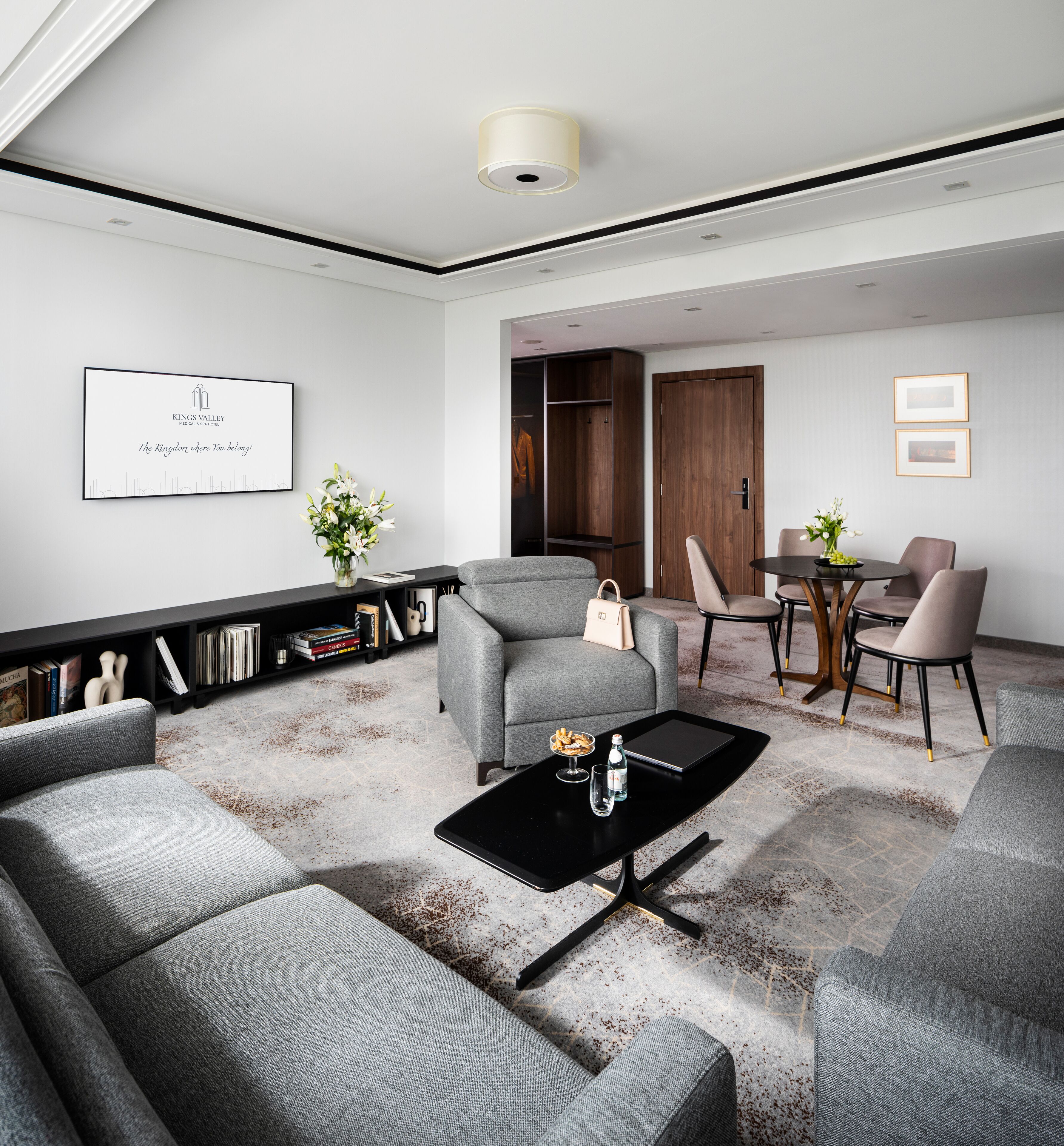 Una sala de estar moderna con un sofá gris, una mesa de centro negra y una estantería con libros y objetos decorativos.