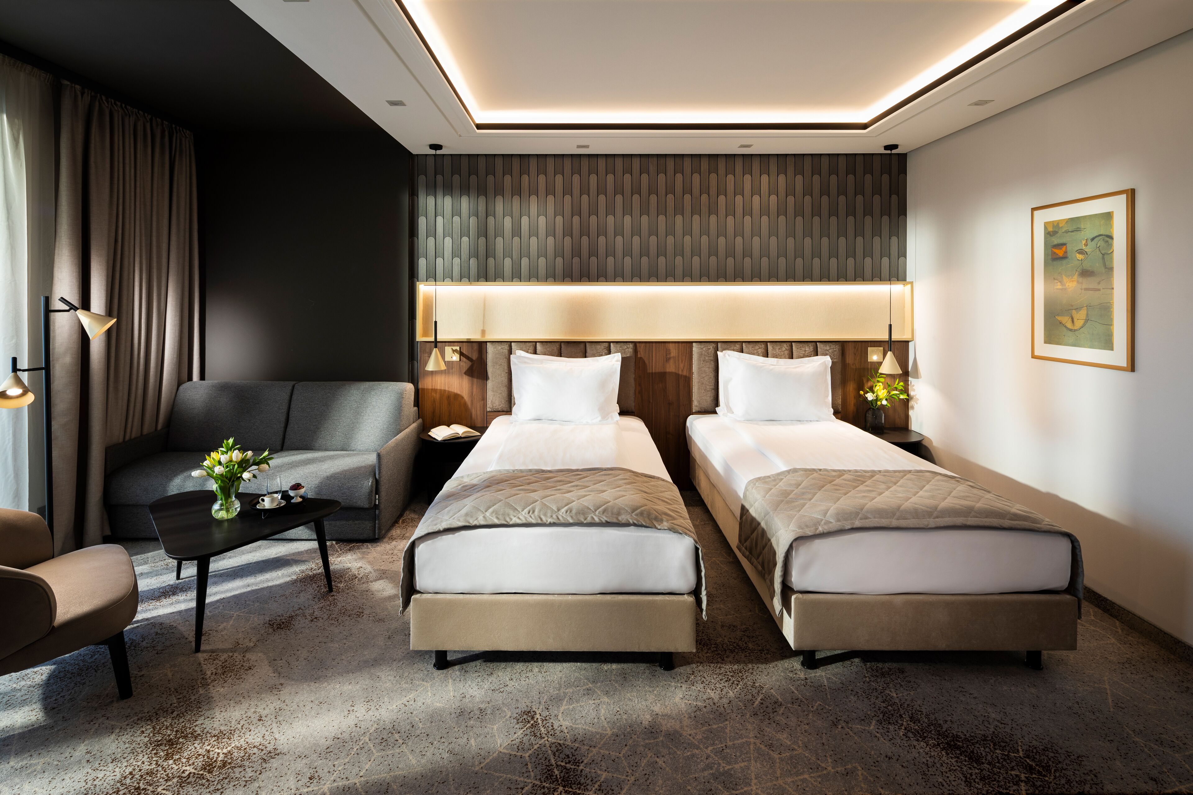 Une chambre d’hôtel avec deux lits, un canapé, une table basse et une lampe.
