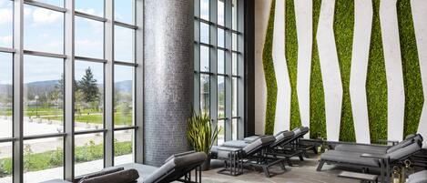 Un área de spa con tumbonas, ventanas amplias y una pared verde.
