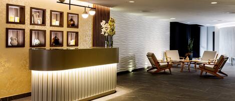 A reception area with a modern reception desk, framed pictures, and a seating area with chairs and a table.