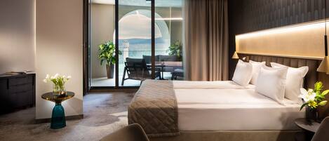 A modern hotel room with a large bed, a desk, and a view of the outdoors through a glass door.