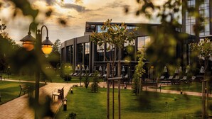 A modern building with large windows, a well-maintained lawn, outdoor seating, and a pathway. - Kings Valley Medical & Spa Hotel (Kazanlak)