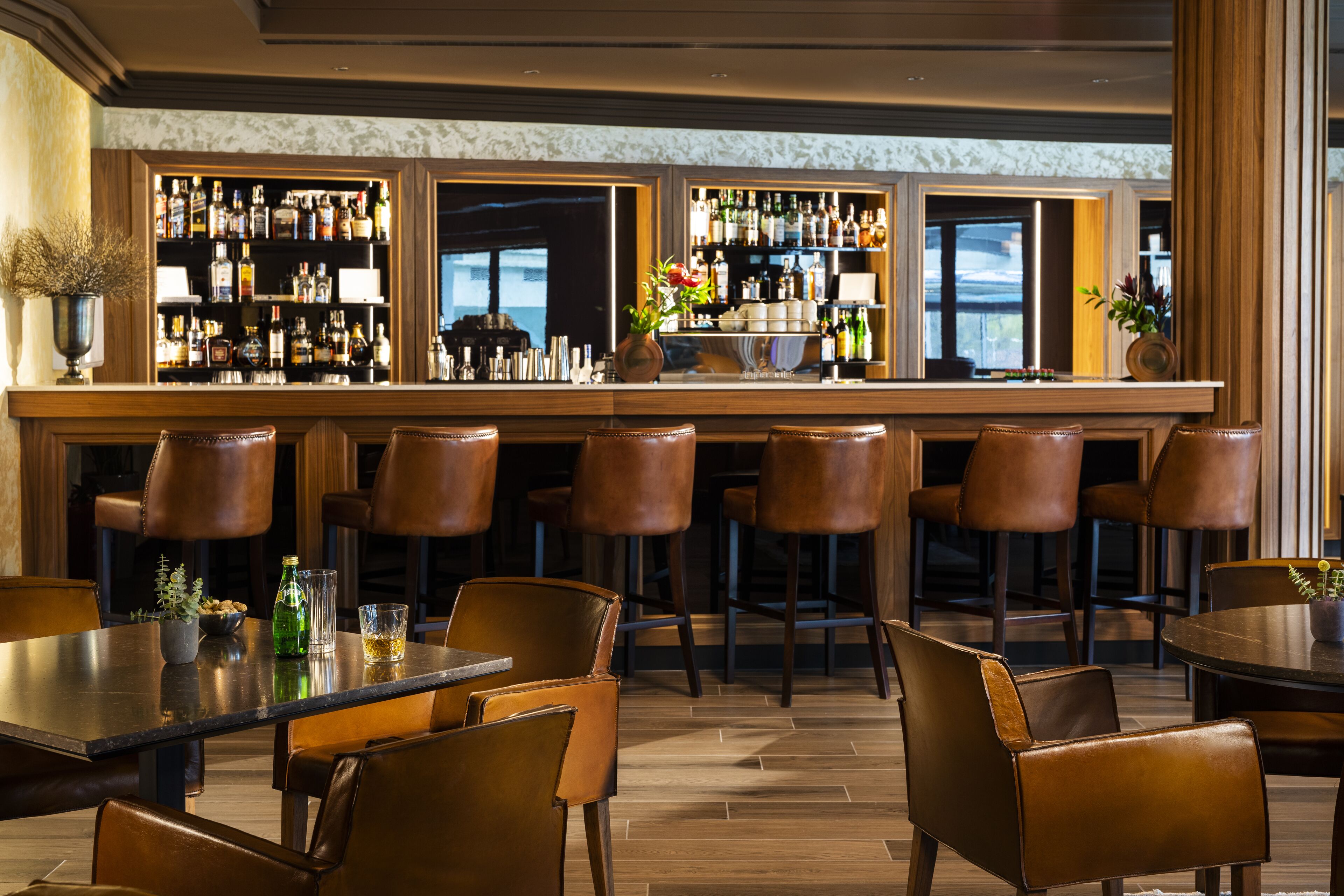 A bar area with multiple stools, a bar counter, and a selection of bottles.