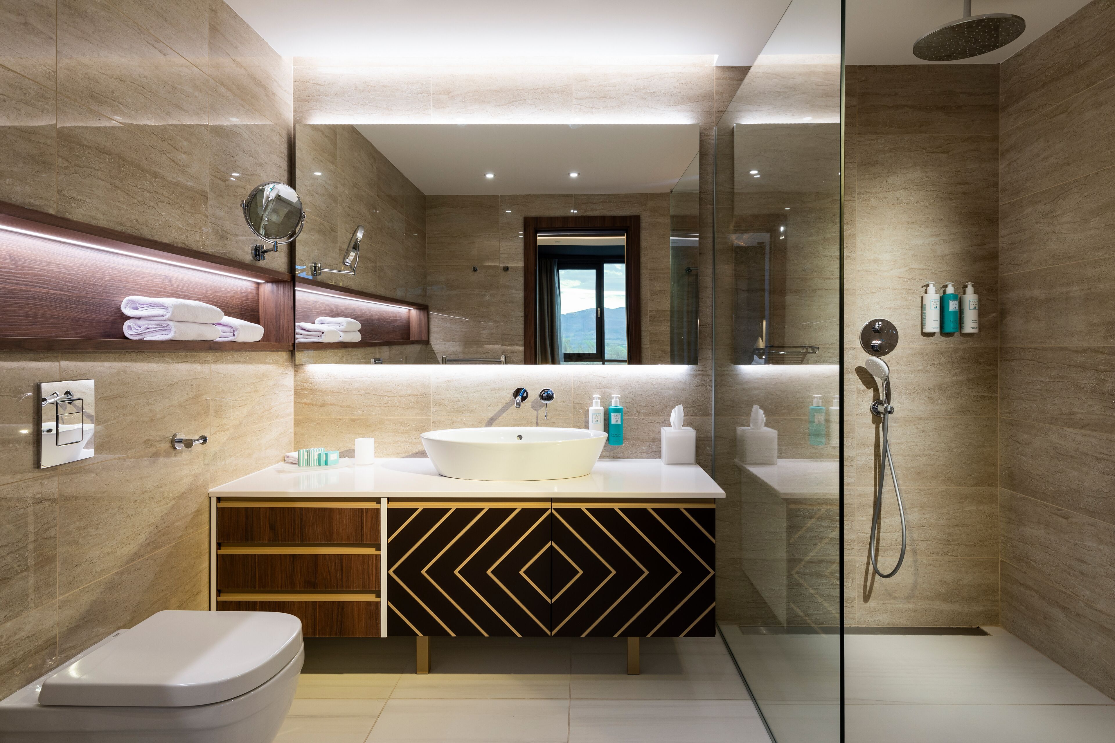 A modern bathroom with a large mirror, a white sink, a toilet, and a shower.