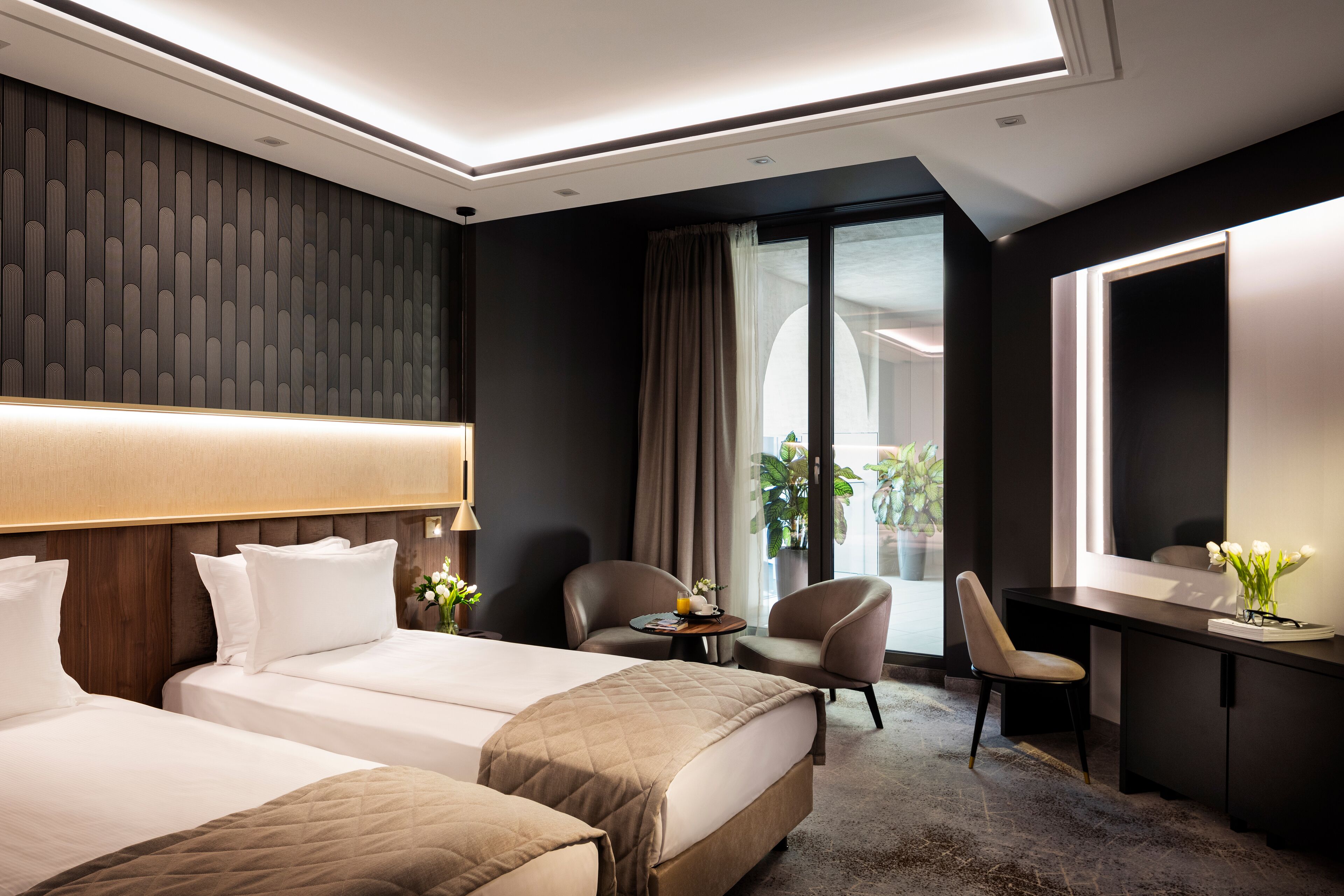 A modern hotel room with two beds, a desk, and a seating area.