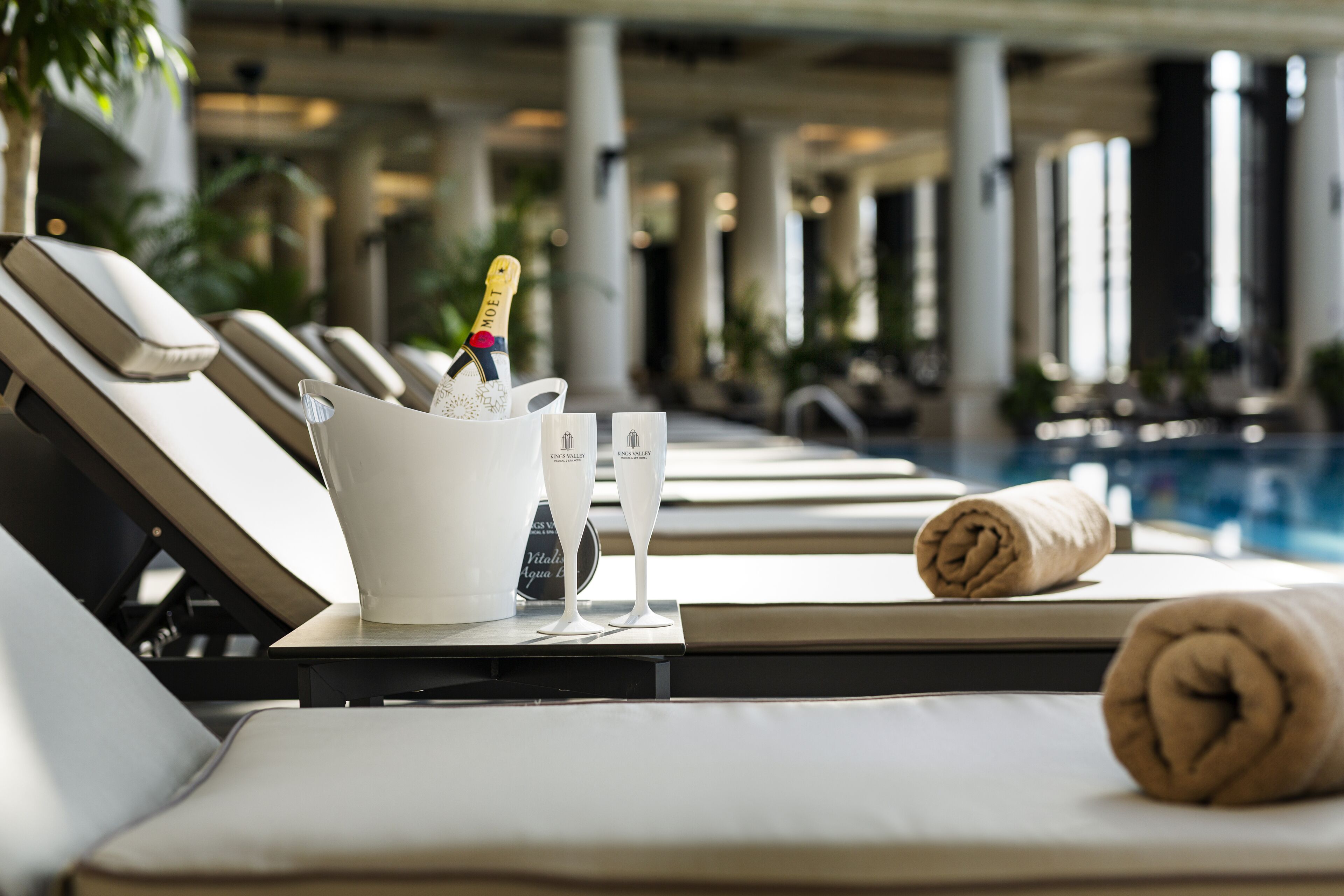 A poolside lounge area with sun loungers, a bucket of champagne, and a rolled towel.