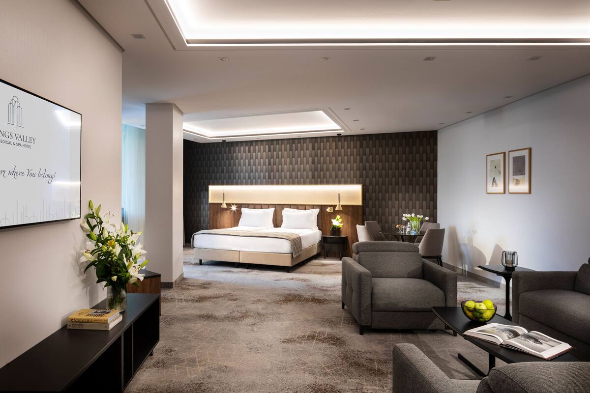 A modern hotel bedroom with a large bed, a sofa, a coffee table, and a desk.