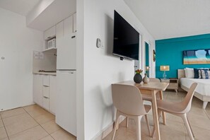 A compact hotel room with a kitchenette, a flat-screen TV, a bed with a blue accent wall, and a dining area. - Imperial Suite | Spacious studio with stunning ocean views! (San Juan)