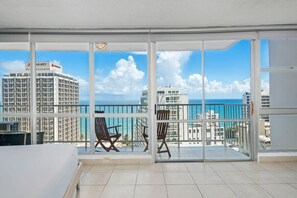 A balcony with two chairs and a table, overlooking a cityscape and the sea. - Imperial Suite | Spacious studio with stunning ocean views! (San Juan)