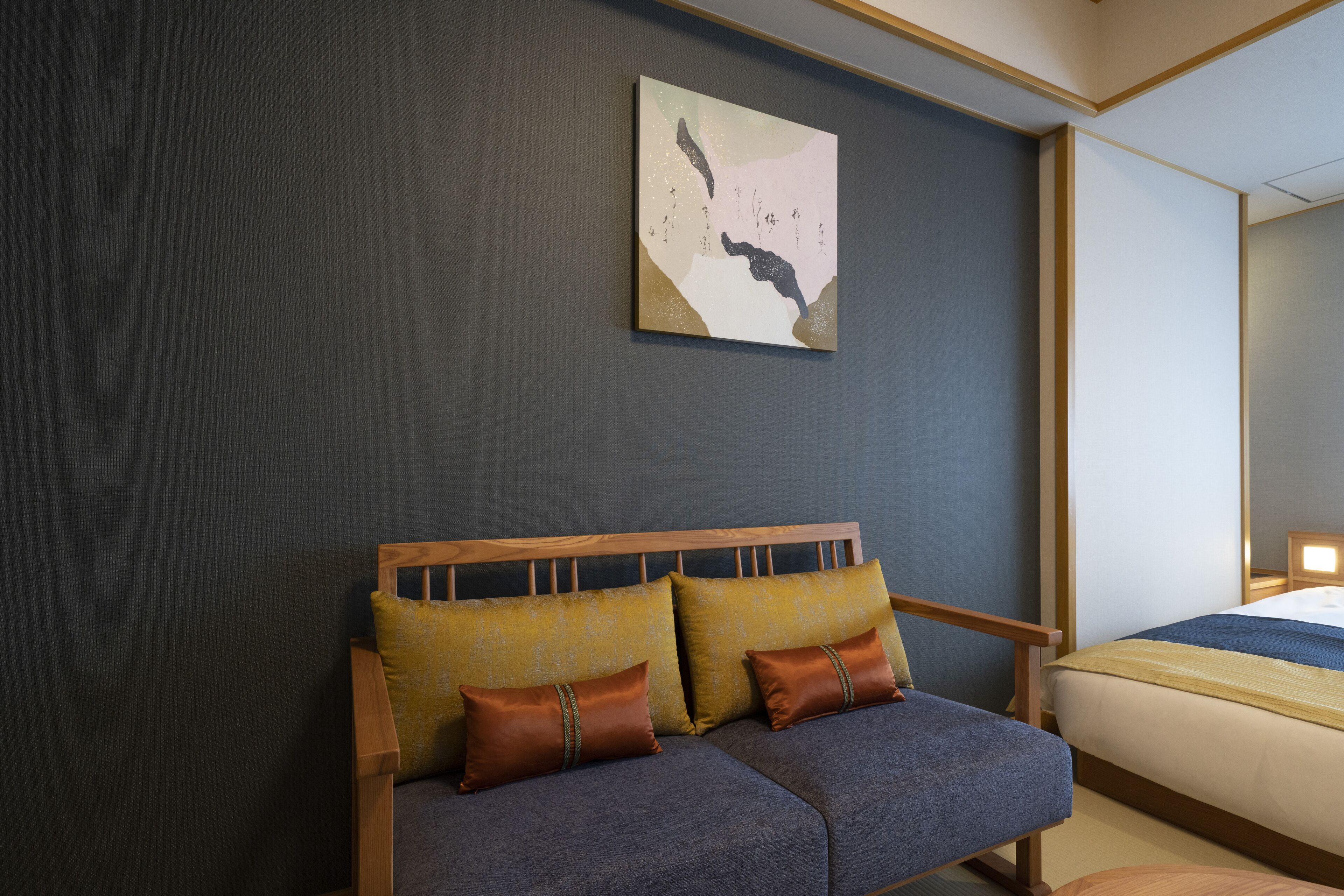 A modern hotel room with a grey sofa, two brown pillows, and a large abstract painting on the wall.