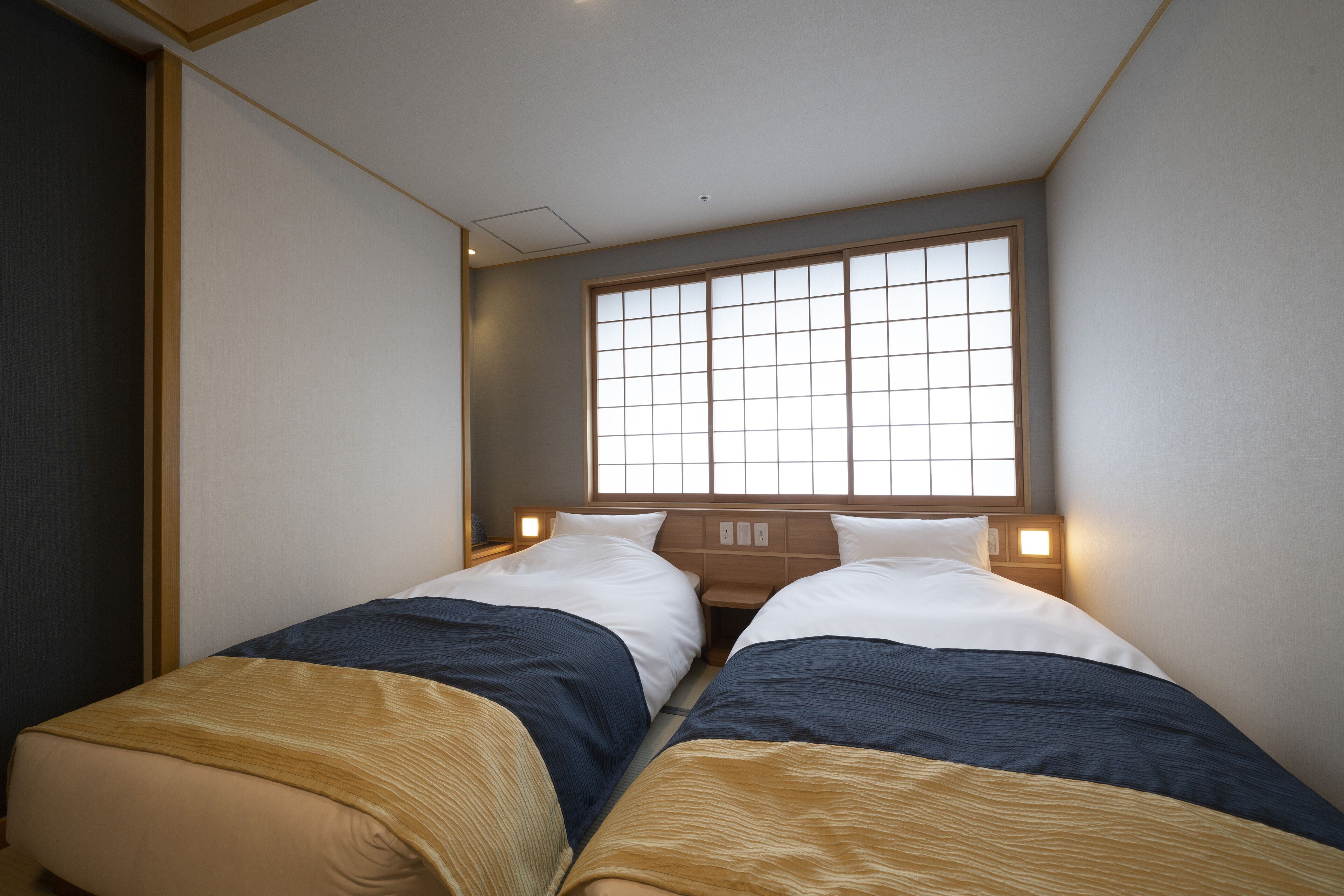 Une chambre d’hôtel avec deux lits, une grande fenêtre à carreaux et une tête de lit en bois.