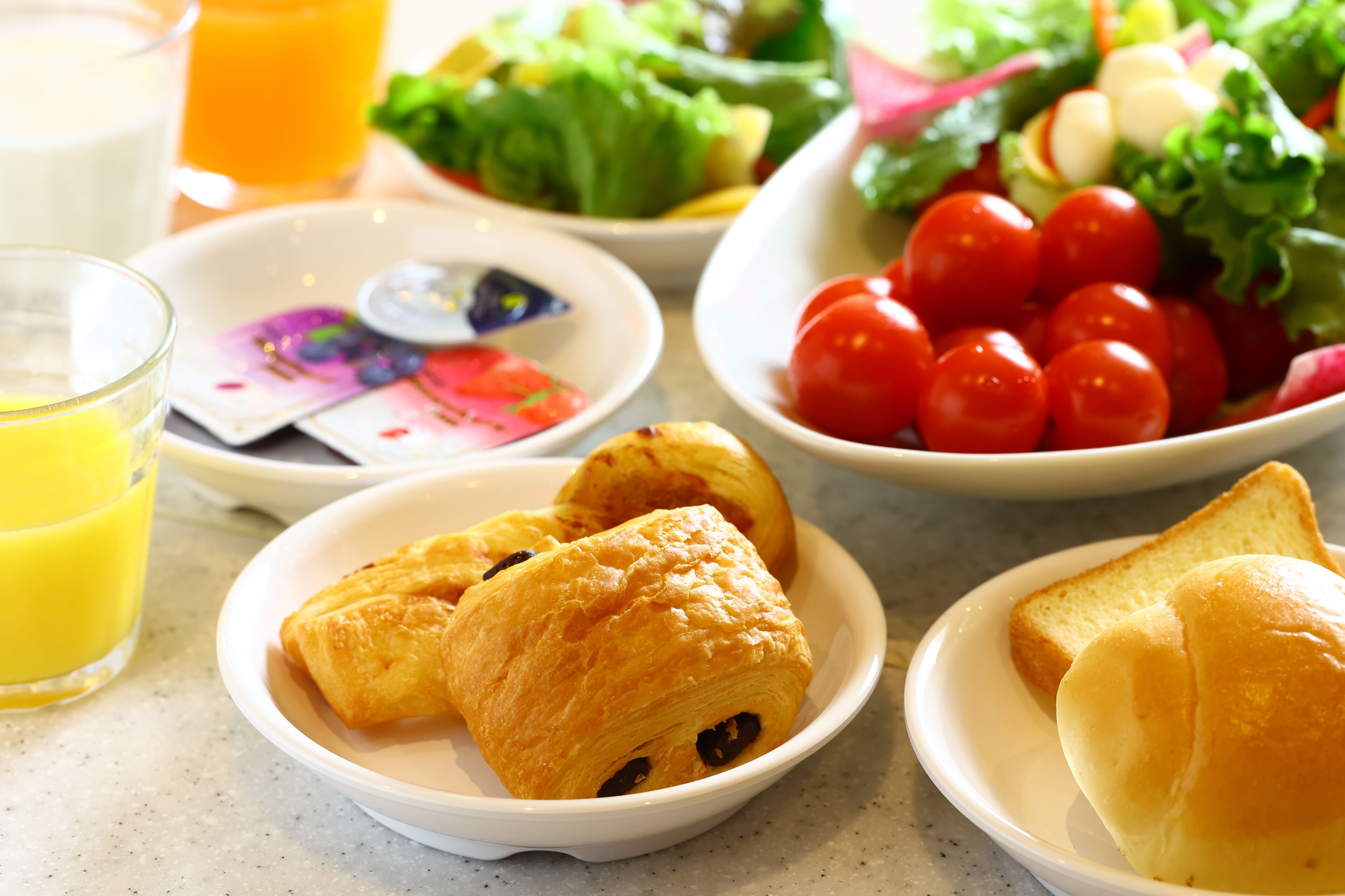 A breakfast setting with croissants, a salad, cherry tomatoes, and a glass of orange juice.